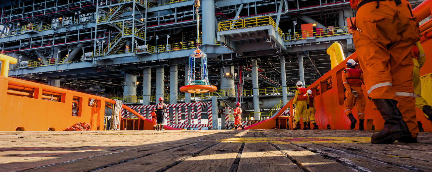 Cesta de carga içada por guindaste entre embarcação de apoio e plataforma offshore durante operação de embarque